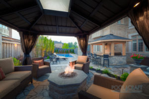 An outdoor living space with a patio, outdoor firepit, couches and outdoor kitchen, designed and installed by Pool Craft