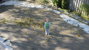 A boy stands on a winter pool cover on top of a backyard swimming pool during the autumn, after the pool has been closed for winter.