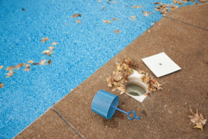Autumn leaves littering an in-ground swimming pool with the skimmer basket emptied on the patio